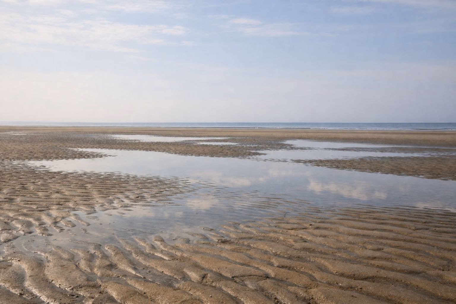 Wide wet sand flat at low tide with shallow puddles and ripple marks