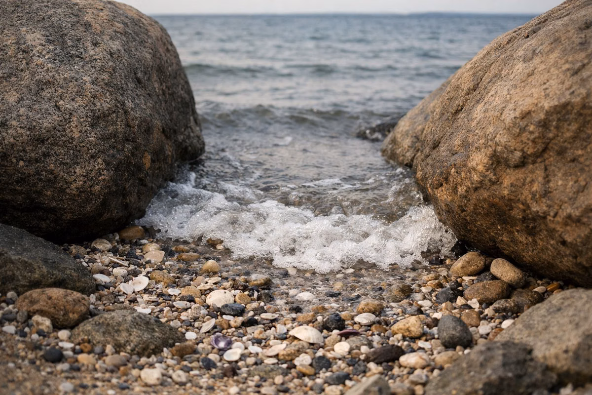 A small wave washing over shells and pebbles between two large boulders